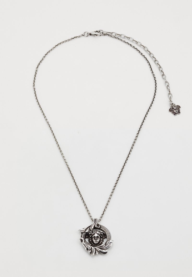 Silver chain necklace featuring a round pendant with a sculpted face and decorative leaf accents, displaying intricate detailing and texture.