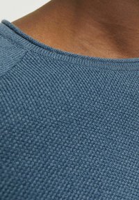 Blå texturerad stickad tyg som visar en närbild av halsringningen med ett subtilt ribbat mönster och slät krage.