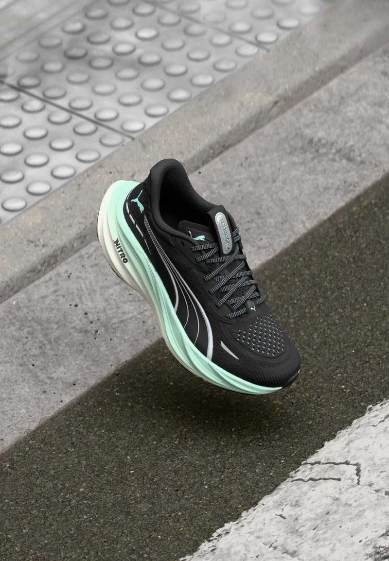 Chaussure de course noire avec un dessus en mesh et des détails réfléchissants, présentant une semelle intermédiaire vert menthe et des accents latéraux, positionnée au-dessus d'une surface texturée.