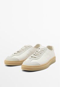 Weiße Wildledersneaker mit runder Zehenform, strukturierten Akzenten und einer beigen Gummisohle. Mit flachen Schnürsenkeln und einem gepolsterten Kragen ausgestattet.