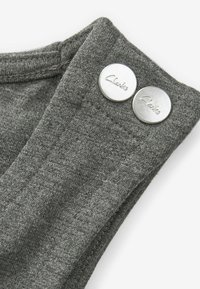 Grijze stof met een gladde textuur, voorzien van twee zilveren knopen met de inscriptie "Clarks" op de bovenrand. Horizontale stikdetails zijn zichtbaar.