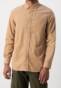 Hellbraunes, langärmliges Hemd mit Knöpfen und spitzem Kragen, ausgestattet mit einem kleinen orangefarbenen Logo auf der Brust und einer weichen Stofftextur.