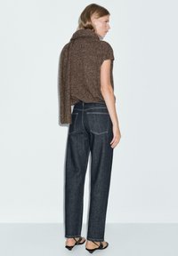 Top in maglia marrone con trama, collo a imbuto, abbinato a jeans a vita alta blu scuro con cuciture bianche e vestibilità rilassata.