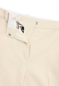 Pantalon en tissu côtelé de couleur crème, avec braguette zippée, fermeture par bouton et poches latérales. Dispose d'une étiquette textile à l'intérieur.