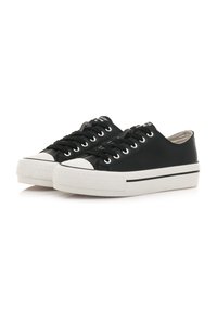 Zapatillas de lona negras con puntera y suela blancas, con cordones y costuras negras, y una delgada franja negra alrededor de la suela.