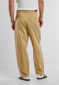 Khaki relaxed-fit trousers with a high waist, two back pockets, and a smooth cotton texture. Worn with white and black sneakers.