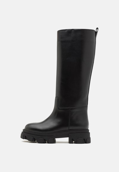 Črne škornje do kolen iz gladke usnje, ki imajo debel in teksturiran podplat ter zadaj zanko za enostavno obuvanje. Minimalističen dizajn.
