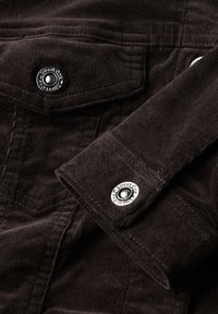 Manche et poche d'une veste en velours côtelé marron foncé avec des boutons-pression argentés gravés du logo "Street One".