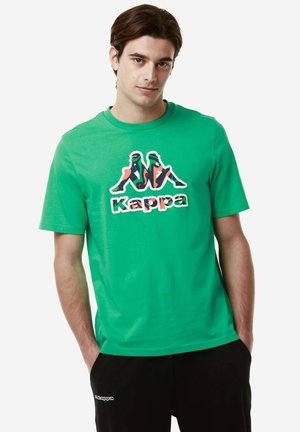 T-shirt verde a maniche corte in cotone, con un logo Kappa multicolore stampato sul davanti su uno sfondo uniforme.