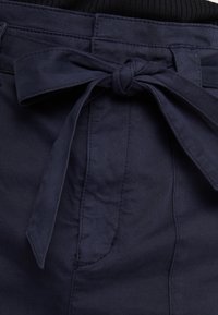 Námořnická modrá páse s mašlí, vyrobená z jemné, hladké tkaniny. Má texturovaný povrch a viditelné stehy.