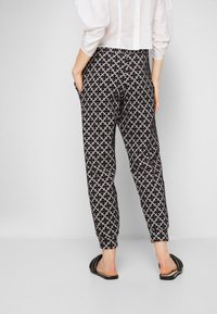 Svart och vit mönstrade byxor med en geometrisk design, med sidofickor och elastiska fållar, kombinerat med svarta slidesandaler.