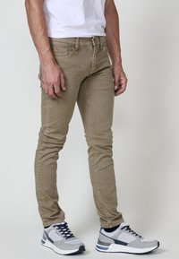 Khaaki skinny farmer nadrág sima textúrával, öt zsebes kialakítással és gombos záródással, szürke és sötétkék sportcipőkkel párosítva.