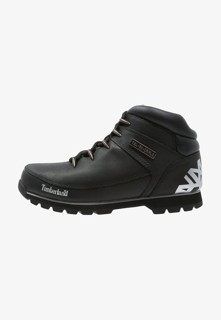 Botte de randonnée Timberland en cuir noir avec œillets métalliques, logo blanc sur le côté et le talon, et semelle épaisse texturée.