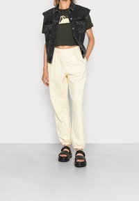 Mustat farkkiliivit lyhyillä hihoilla, oliivinvihreä lyhyt t-paita, vaaleanbeiget jogger-housut ja mustat sandaalit, joissa on solkiyksityiskohta.