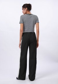 Schwarze weit geschnittene Hose mit einem hellgrauen Seitenstreifen, kombiniert mit einem schwarz-weiß gestreiften Kurzarmshirt. Glatter Stoff und lässige Passform.