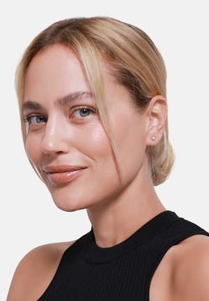 Silberne Steckerohrringe an einem hellhäutigen Modell mit blauen Augen und glattem, blondem Haar, das ein schwarzes, ribbeliges, ärmelloses Oberteil trägt. Glatte Hautstruktur.