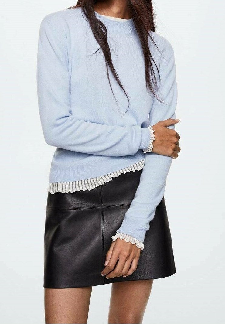 Pull bleu clair avec texture côtelée et bord blanc froncé aux poignets et à l'ourlet, associé à une mini-jupe en cuir noire.