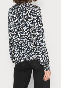 Blusa nera con stampa leopardata blu e bianca, maniche lunghe e polsini arricciati. Tessuto morbido e liscio con una vestibilità rilassata.