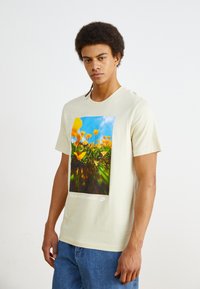 Tricou din bumbac crem cu un imprimeu floral colorat și textul "Mergi cu natura." Are mâneci scurte și guler rotund.