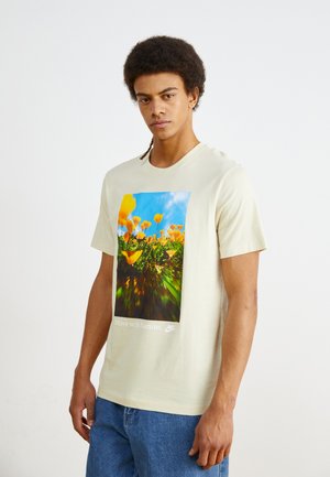 Cremfarbener Baumwoll-T-Shirt mit einem bunten floralen Grafikdruck und dem Text "Bewege dich mit der Natur." Verfügt über kurze Ärmel und einen Rundhalsausschnitt.
