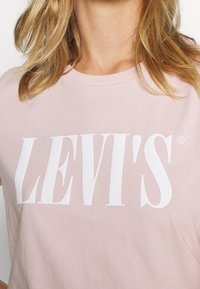 Camiseta de algodón de color rosa claro con un gran logo en blanco "LEVI'S" en una fuente negrita. Cuello redondo y mangas cortas. Textura suave.