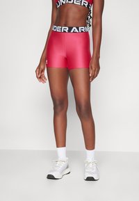 Rote Sportshorts mit glatter Oberfläche, ausgestattet mit einem schwarzen Bund mit "Under Armour"-Logo, kombiniert mit hellgrauen Sneakers und weißen Socken.