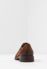 Chaussure en suede marron avec un bout lisse et arrondi et un talon légèrement surélevé. Présente un dessus cousu et une semelle en caoutchouc texturée.