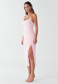 Pink tætsiddende kjole med justerbare spaghetti-stropper, rynket tekstur og høj sideslids. Glat stof med en kropsnær silhuet.