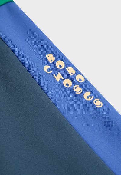 Višebojna atletska tkanina s tamnozelenim dijelom, plavim panelom i svijetlosmeškim tekstom "BOBO CHOSES" duž šava.