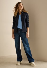 Marineblaue Zip-Jacke, hellblaues V-Ausschnitt-Shirt und lockere dunkelblaue Jeans mit weißen Sneakers; bequemer Schnitt und lässiges Design.