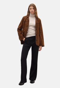 Brown suede jacket with a relaxed fit, black trousers, and a light beige turtleneck. Shoes are black with a rounded toe.