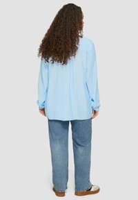 Lichtblauw langarmshirt met een losse pasvorm, textuurstof en verlaagde schouders, gecombineerd met vervaagde blauwe jeans en casual schoenen.