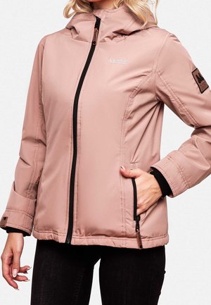 Femme portant une veste à capuche rose clair avec une fermeture éclair noire et des poches latérales, debout avec une main dans la poche.