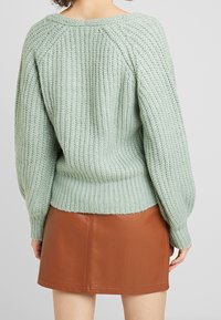 Mintgrön stickad tröja med ett texturerat mönster, ribbade ärmändar och fåll, kombinerad med en bruna fusk läder minikjol.