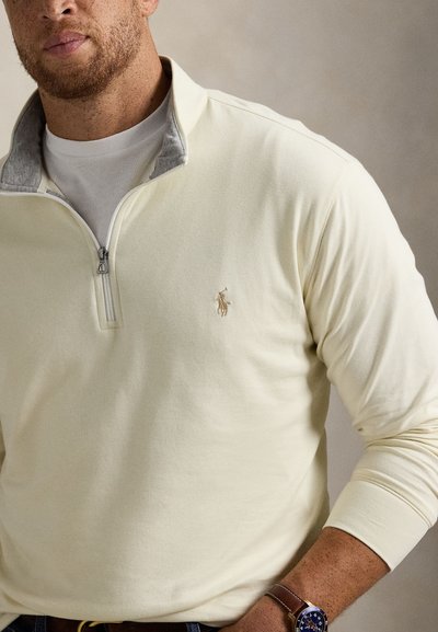 Ανοιχτό κίτρινο πουλόβερ με φερμουάρ τέταρτου μήκους, γκρι γιακά και κεντημένο λογότυπο. Μαλακό υλικό, μακριά μανίκια και φερμουάρ στη λαιμόκοψη.