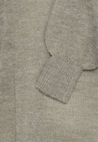 Manche de pull beige en tricot avec détail de bord-côte, montrant la texture et le motif du tissu en laine douce.