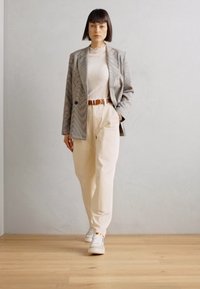 Grijs en witte gestreepte blazer over een licht geribbeld topje, crème broek en witte sneakers. Bruine riemdetails, minimalistisch ontwerp en relaxed fit.