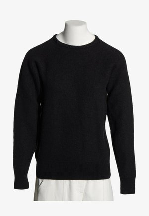 Pull noir à manches longues et col rond, présenté sur un torse de mannequin blanc avec un pantalon beige visible en bas.
