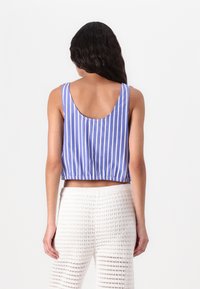 Top corto a righe verticali blu e bianche, con schiena scozzata e orlo elastico. Abbinato a pantaloni bianchi all'uncinetto.