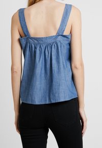 Niebieski top z chambray na ramiączkach o szerokich paskach, z wciąganym detalem z tyłu oraz luźnym krojem. W komplecie z czarnymi spodniami, prezentującymi swobodny styl.