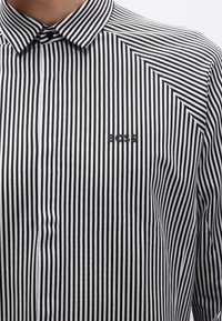 Melna un balta svītraina krekls ar klasisku apkakli, kreisajā pusē neliels melns "BOSS" logotips, gluda kokvilnas auduma.