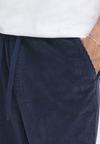 Tmavě modré manšestrové kalhoty s vertikálním žebrováním, s nastavitelným šňůrkovým pasem a bočními kapsami, s měkkou texturou.