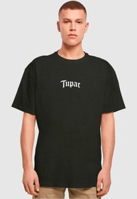 Black cotton t-shirt with short sleeves and a round neck, featuring white text "Tupac" in a stylized font centered on the front.