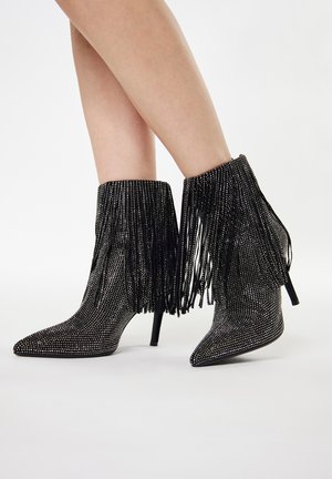 Zwarte enkelboots met spitse neuzen, bedekt met zilveren rhinestones, met lange zwarte franjes langs de bovenkant, gezet op een stiletto hak.