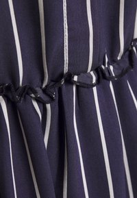 Tessuto a strisce blu navy e bianche con una superficie morbida e texturizzata. Presenta dettagli arricciati con bordi arruffati lungo la cucitura.