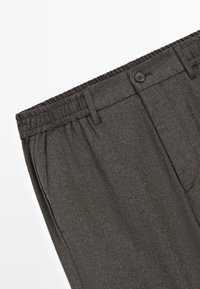 Pantaloni grigi in tessuto intrecciato con vita elastica, passanti per la cintura e bottone frontale. Presentano tasche laterali e una superficie liscia.