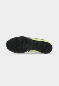 Semelle en caoutchouc texturée noire d'une chaussure de sport jaune et grise Puma avec des points d'adhérence et le logo Puma au centre.