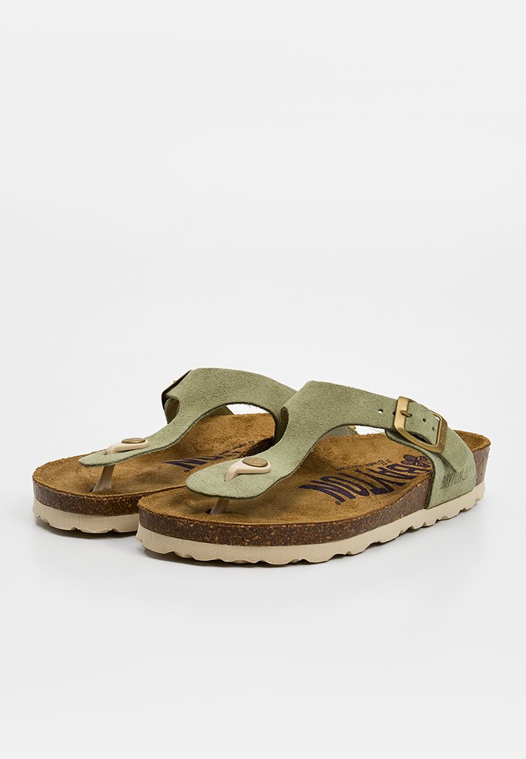 Paar olivgrüne Sandalen aus Wildleder mit verstellbaren Riemen und Korksohlen auf beigen Sohlen.