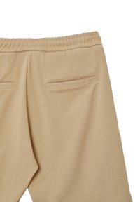 Pantaloni della tuta beige con un tessuto testurizzato, vita elastica e due tasche posteriori con aperture orizzontali eleganti.
