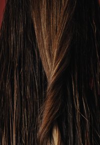 Långt, vågigt hår med mörkbruna och ljusare karamelltonade slingor, med en glansig textur. Sektioner tvinnade tillsammans nära bakdelen.